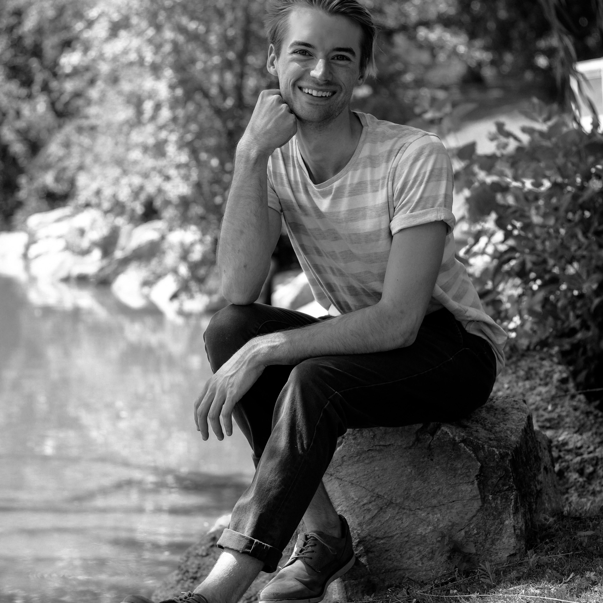 Photo of Caleb sitting on a bench outside in black and white