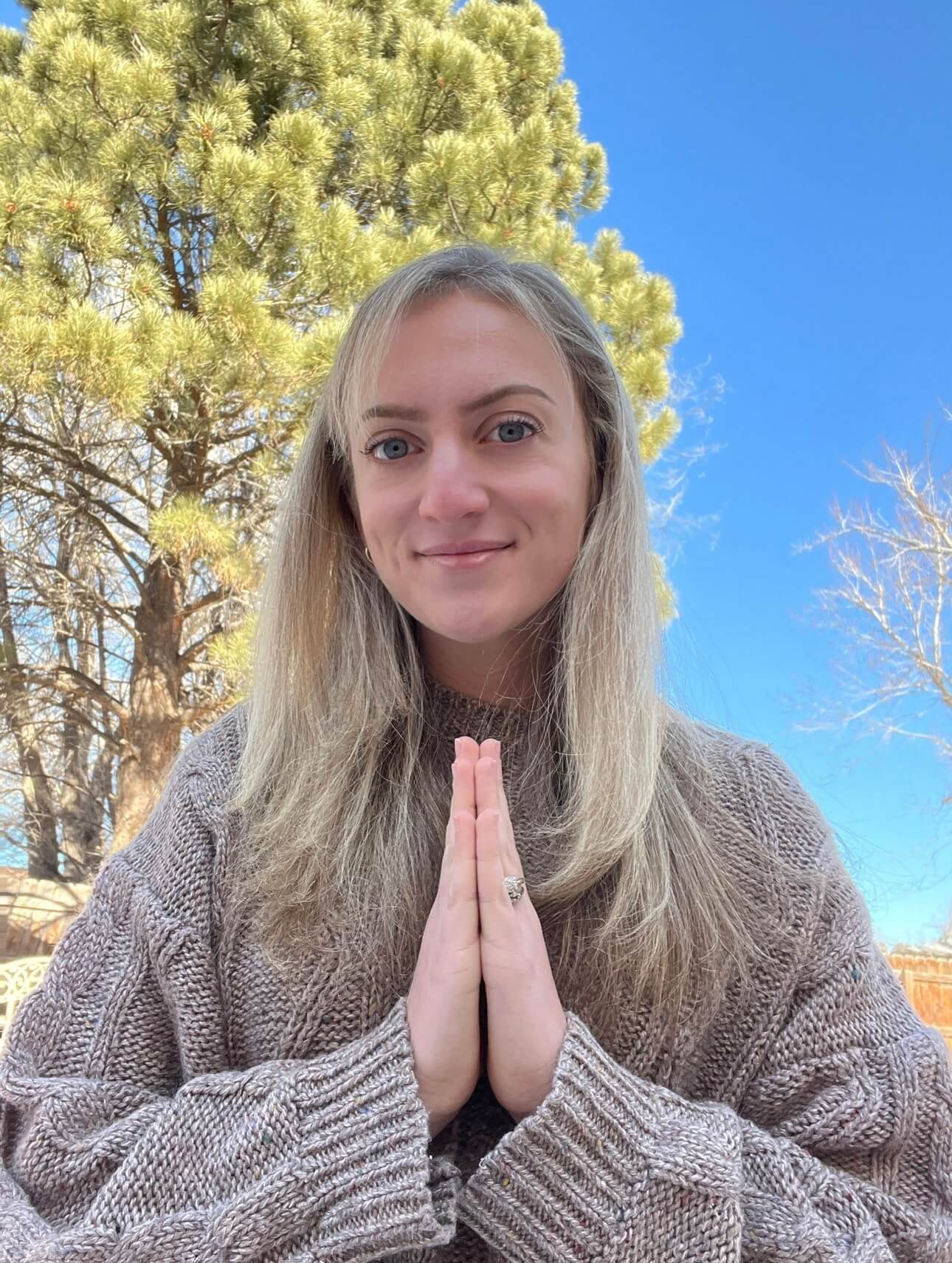 Photo of Sarah outside with a clear blue sky and her hands at hear center